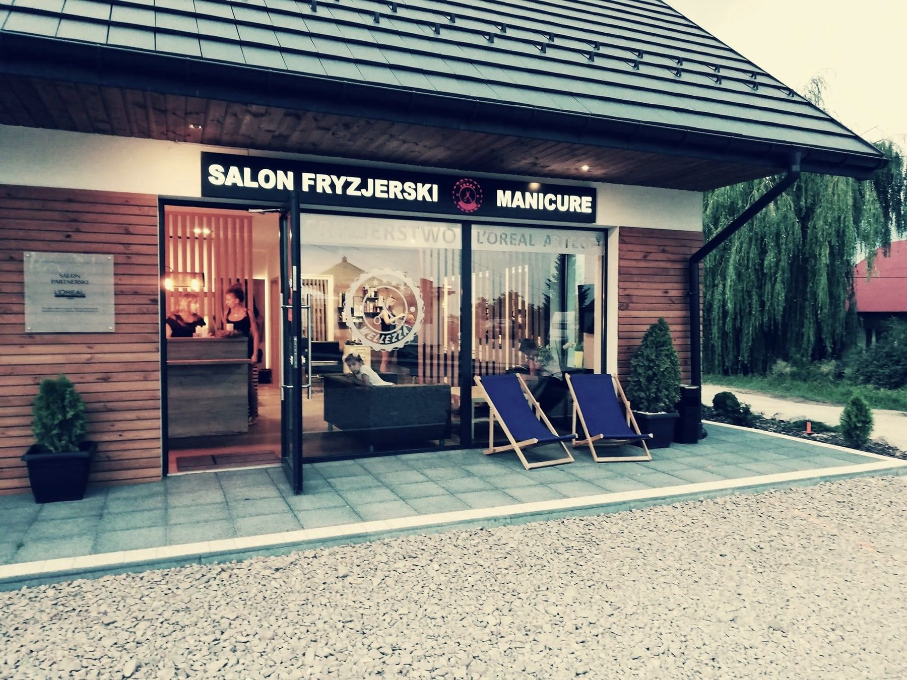 Pawilon salonu Wellezza przy ul. Ochota 9a w Wieliczce: drewniane deski, szyld z logo, leżaki przed wejściem